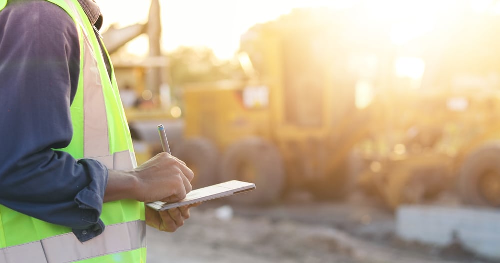 Construction engineer using a tablet on-site with heavy machinery in the background.